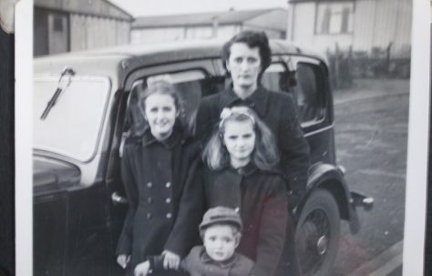 Woman with three children in front of car and prefabs