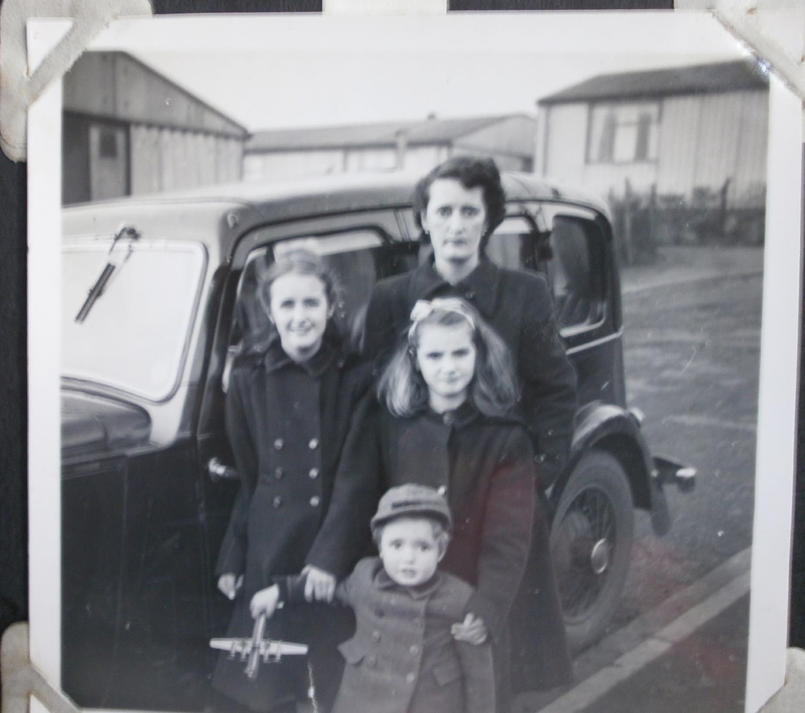 Woman with three children in front of car and prefabs