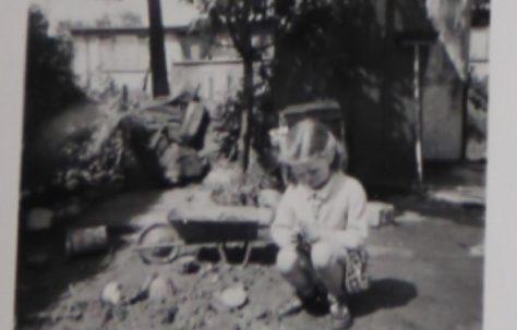 Penny Bishop as a small child playing with a toy wheelbarrow in the prefab garden