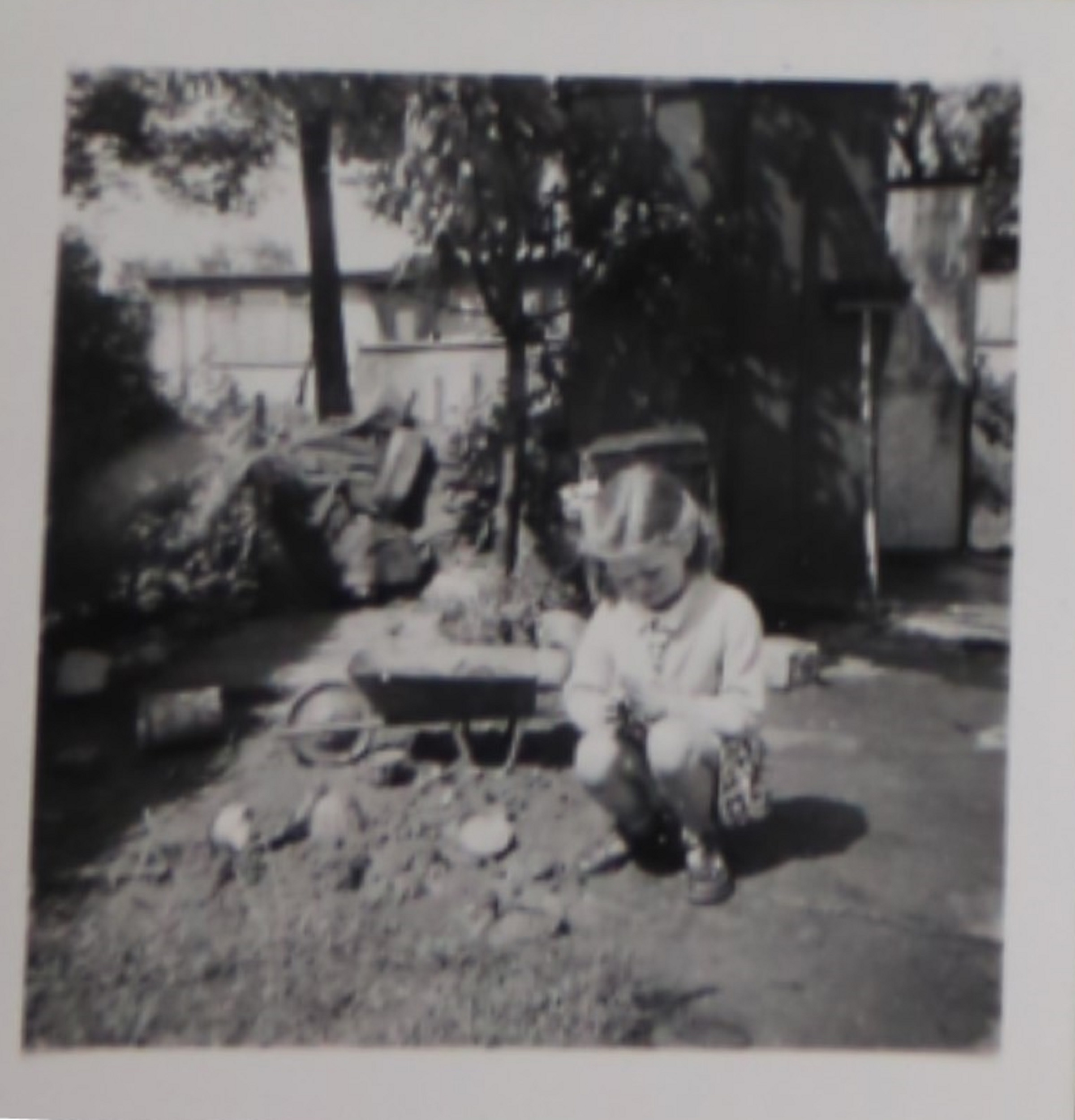 Penny Bishop as a small child playing with a toy wheelbarrow in the prefab garden