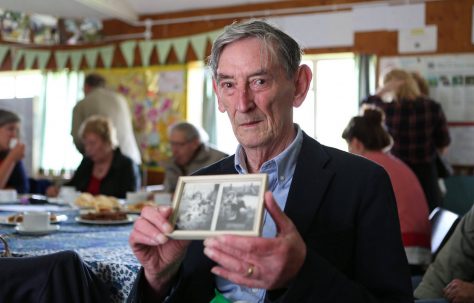 Ray Smith holding photos of his family prefab in Penarth, South Wales at the Excalibur at 70 event, 2016