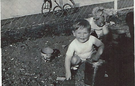 Two small children playing in the prefab garden, one in background on bike. Clement Road, Willesden