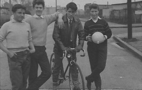 Four teenage boys, one on a bike, in front of prefabss. Stewart Street, London E14