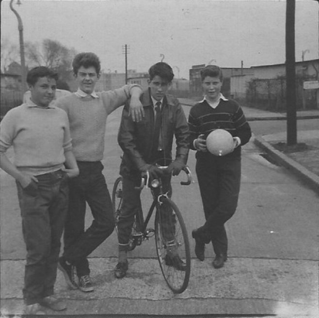 Four teenage boys, one on a bike, in front of prefabss. Stewart Street, London E14