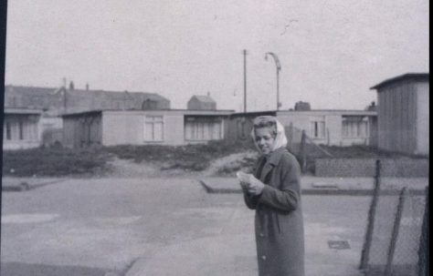 Woman standing in street in front of prefabs. Stewart Street, London E14