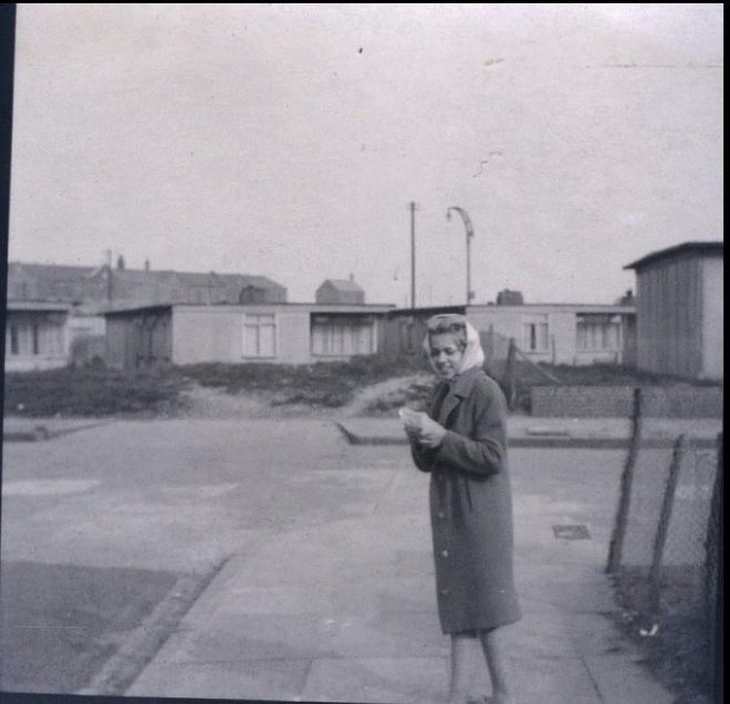 Woman standing in street in front of prefabs. Stewart Street, London E14