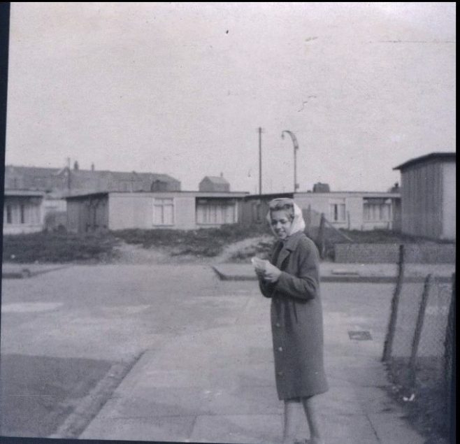 Woman standing in street in front of prefabs. Stewart Street, London E14
