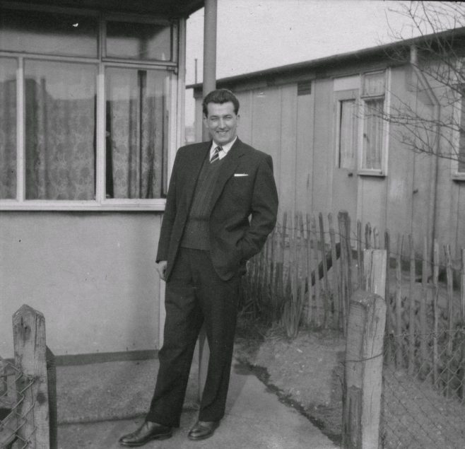 Man In suit standing in front of prefab.  Stewart Street, London E14