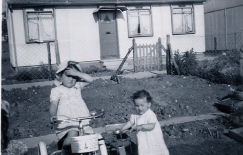 Two little girls, one on a bike, in front of a prefab on the Harold Hill estate