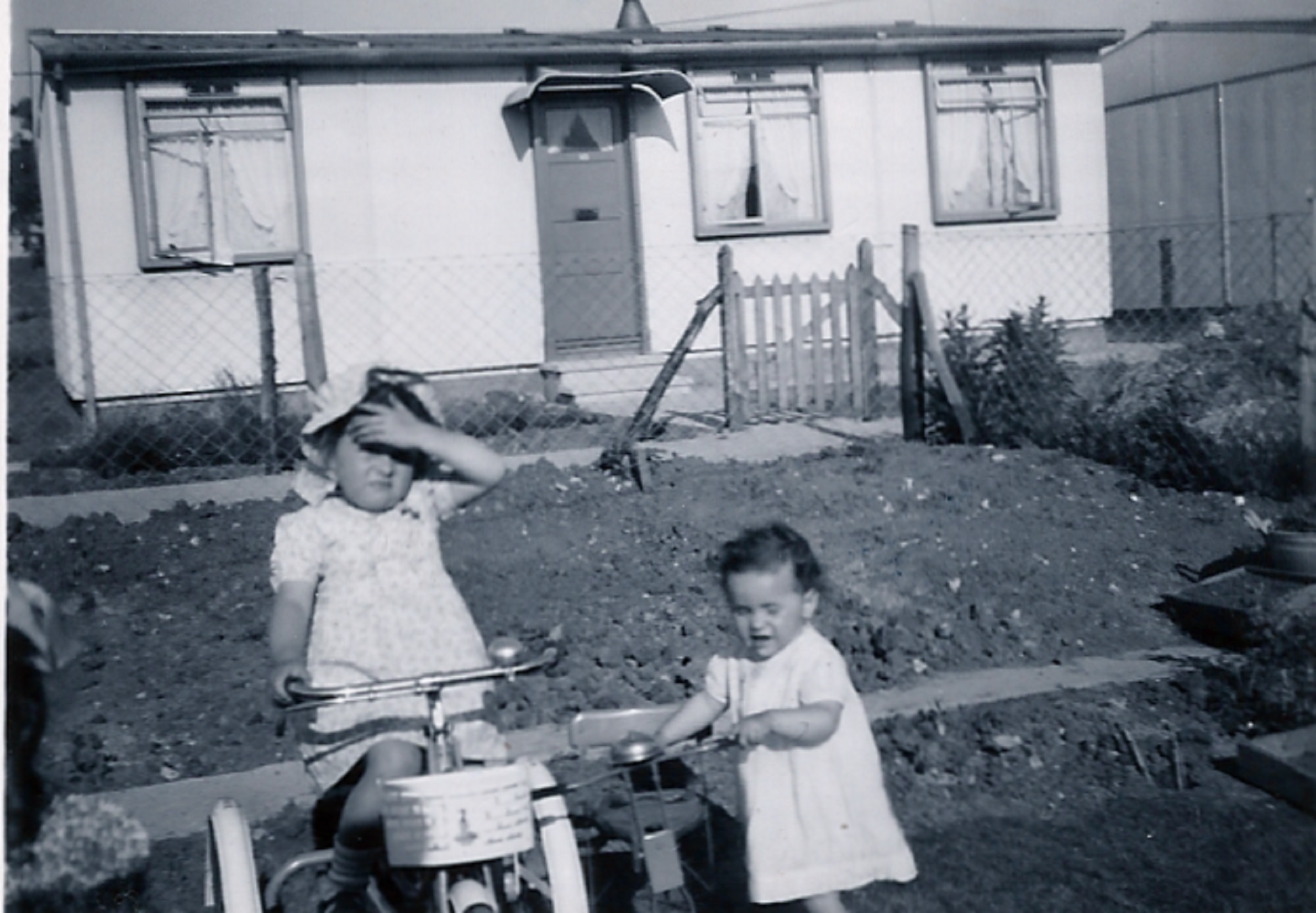 Two little girls, one on a bike, in front of a prefab on the Harold Hill estate