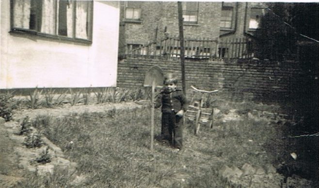 Alf with a big shovel and bike in the prefab garden at Narford Road, London E5
