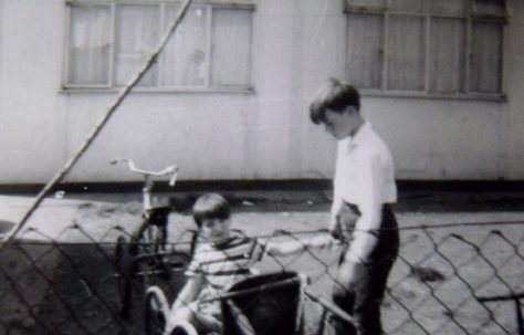 Two boys, one in a bicycle trailer, outside the prefab at Underhill Road, London SE22