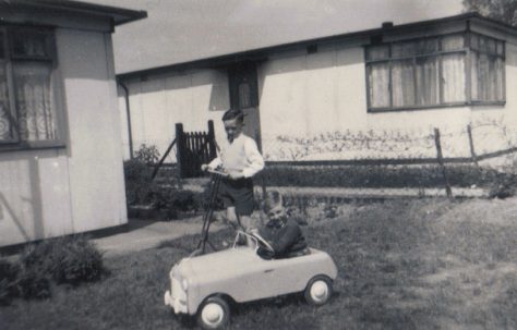 Terence on his scooter and neighbour Raymond in toy car in the prefab garden, Dartmouth Park Hill, London NW5