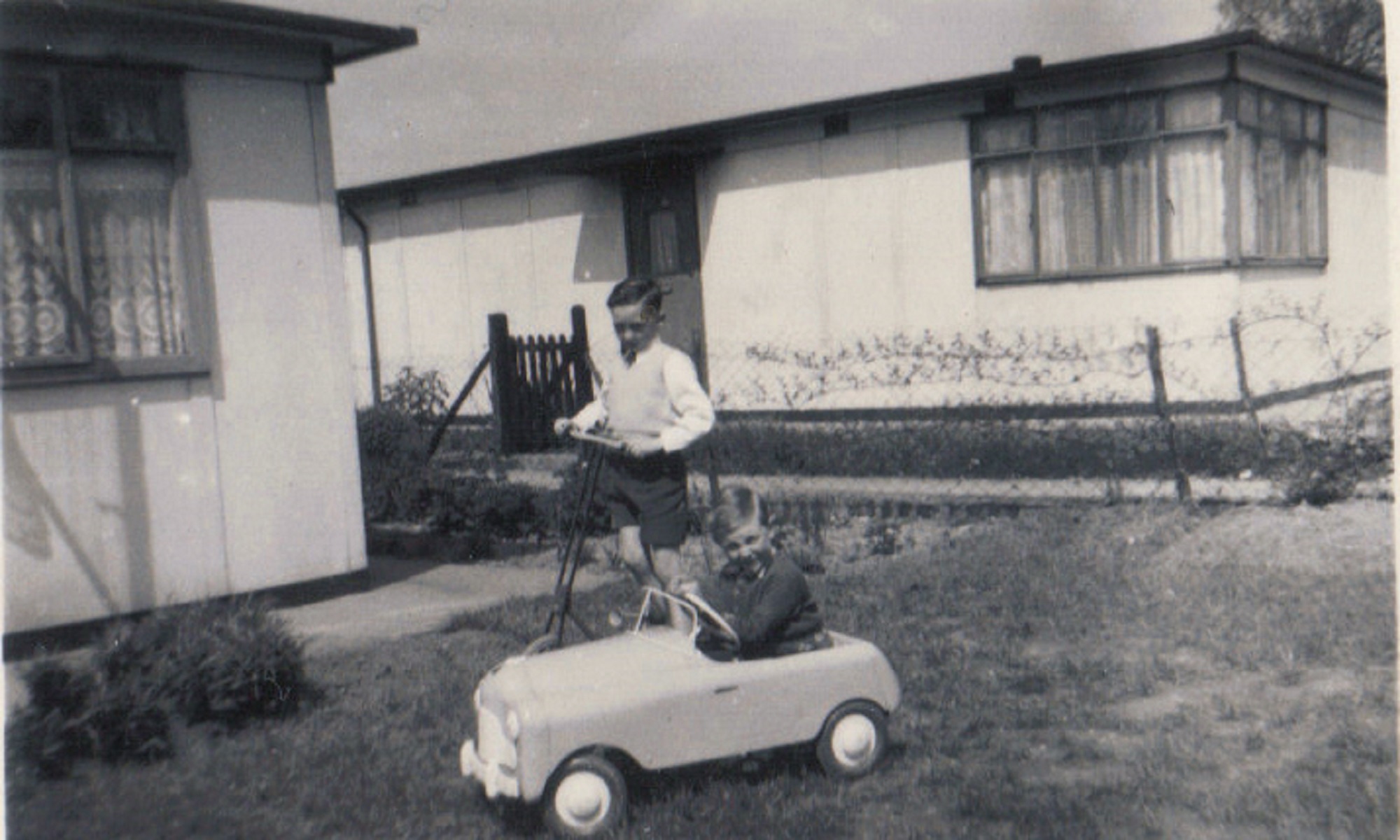 Terence on his scooter and neighbour Raymond in toy car in the prefab garden, Dartmouth Park Hill, London NW5