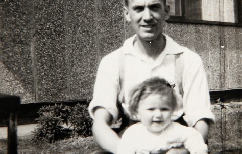 Dad with baby outside Tarran prefab. Bolsover, Derbyshire