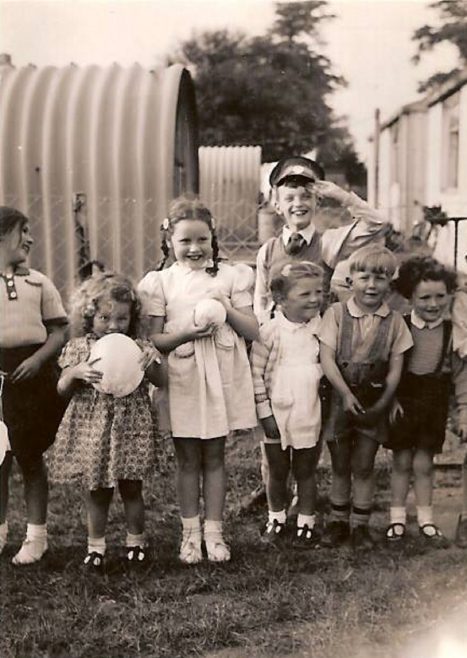 Seven smiling children by the coal shed. Hollyhedge bungalows, Blackheath, London SE3