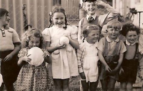 Seven smiling children by the coal shed. Hollyhedge bungalows, Blackheath, London SE3