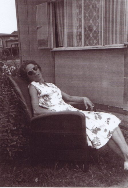 Jim's mum sitting in a chair in the prefab garden. Excalibur Estate, London SE6