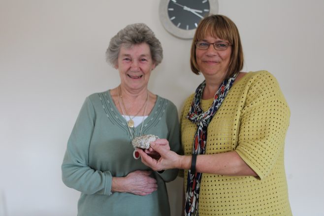 Portrait of Peggy holding a piece of her old prefab, with Siobhan from Rykneld Homes